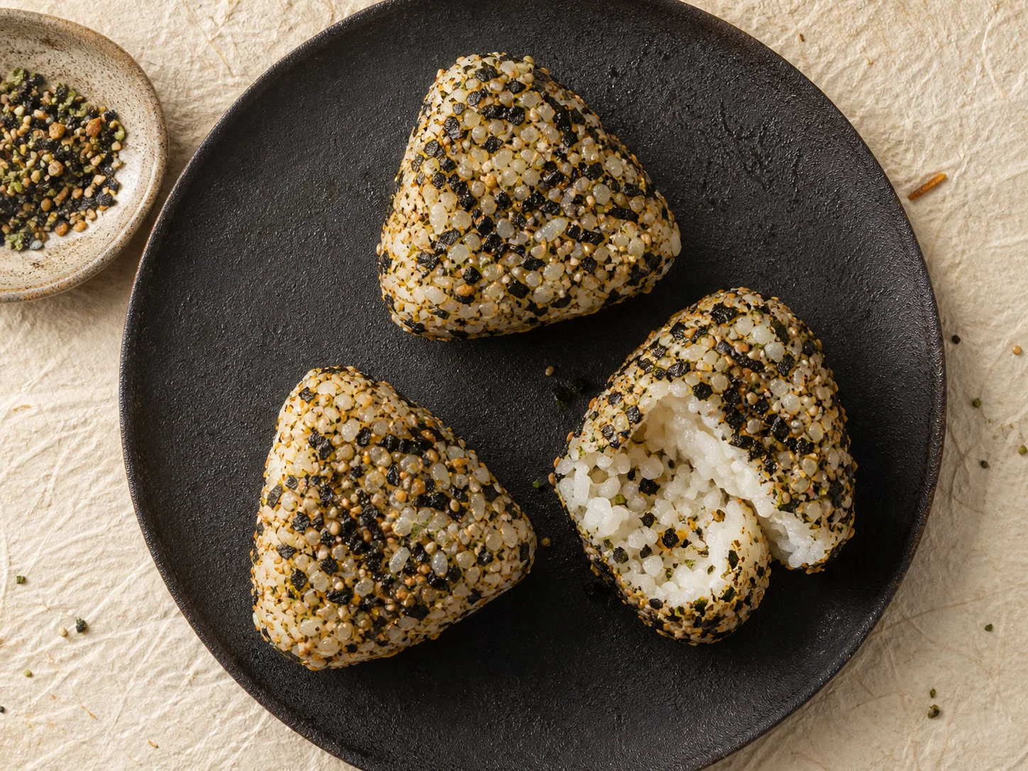 Three furikake-covered onigiri on a dark ceramic plate